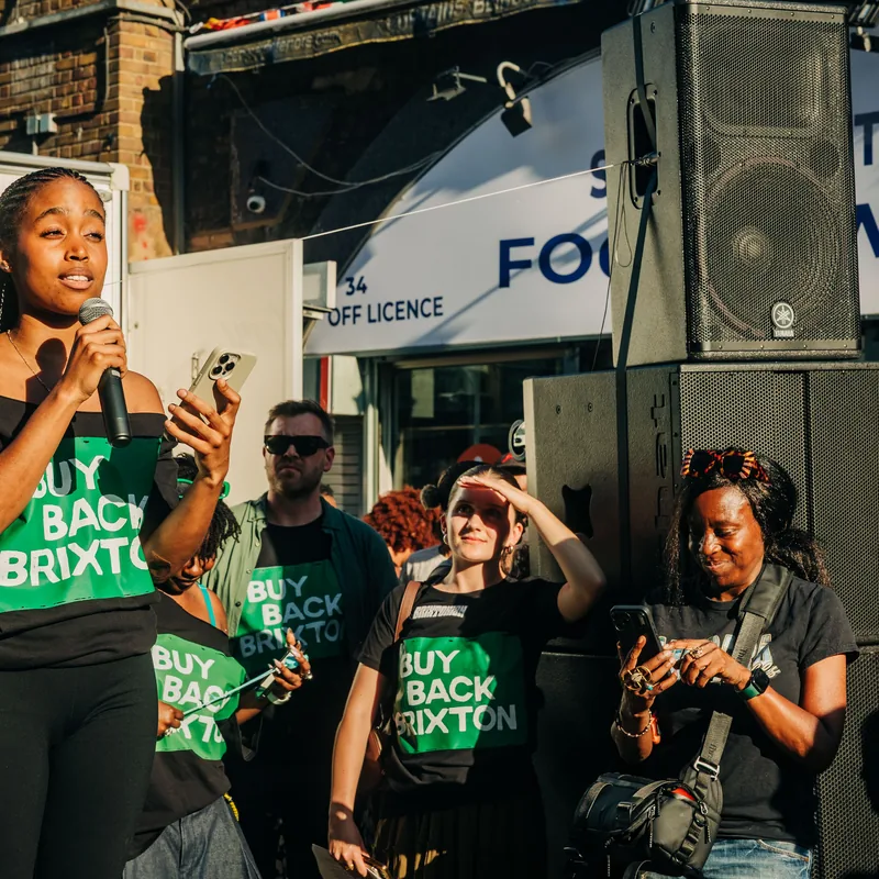 A campaigner on stage addressing the rally with a microphone, supporters watching from the street below.