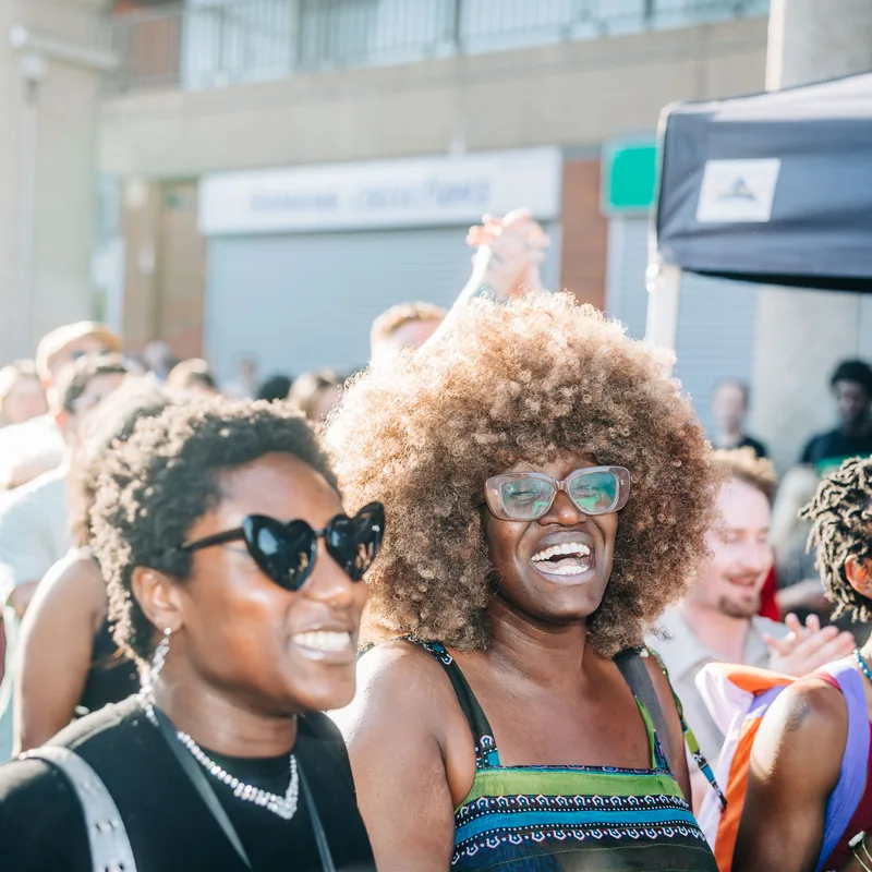 Two women laughing together in the crowd at the rally, sunglasses on in the summer light.