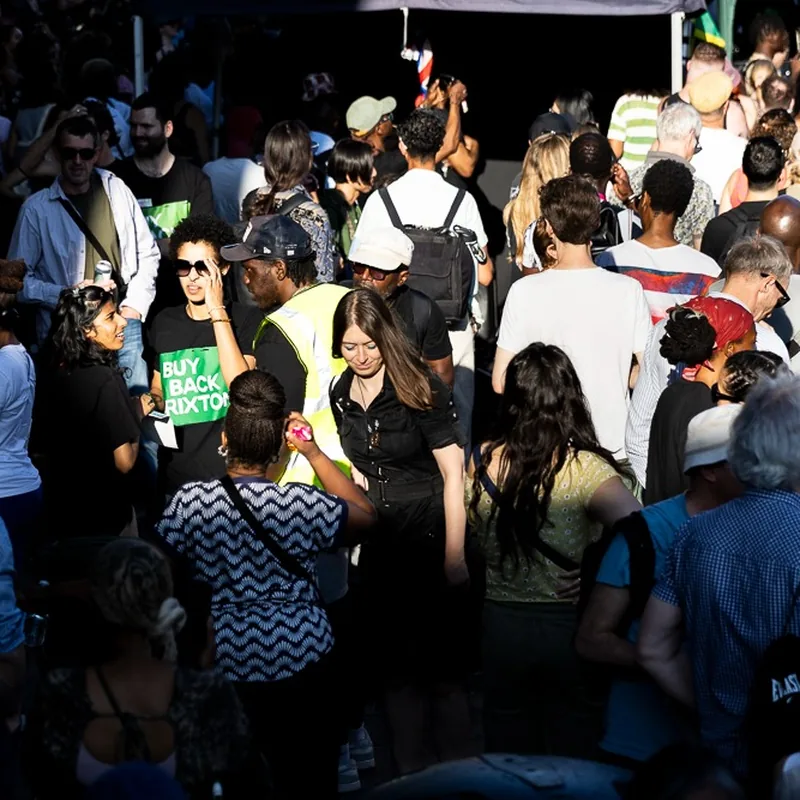 A dense crowd at the rally in the evening light, a Buy Back Brixton T-shirt in the middle of it.