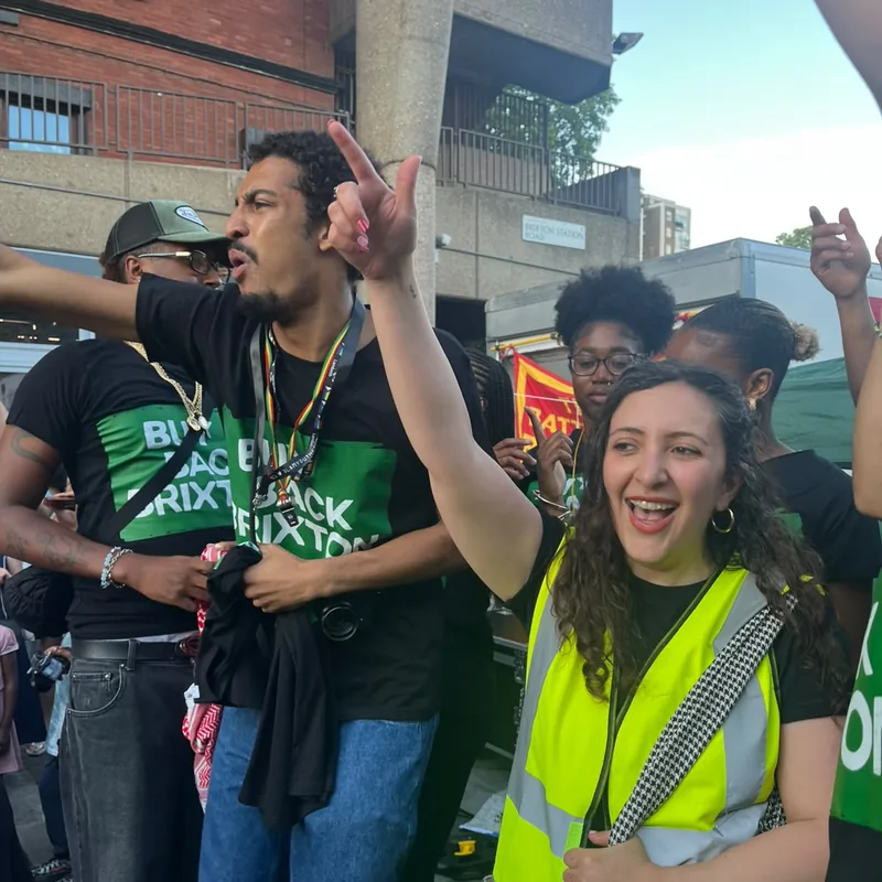 A supporter mid-chant beside a steward in a high-visibility vest.