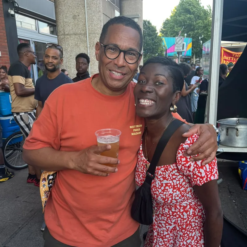 Two supporters laughing together in the crowd, one holding a drink.
