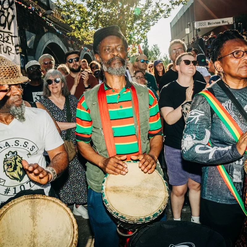 Drummers playing djembes to the crowd, one wearing red, gold and green.
